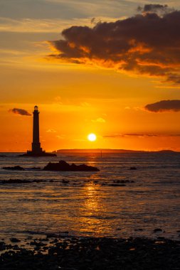 Deniz fenerini ve okyanus dalgalarını aydınlatan altın gün batımı