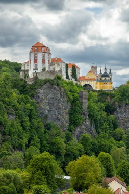 Dramatik gökyüzü altındaki yemyeşil orman manzarasına bakan tarihi şato.