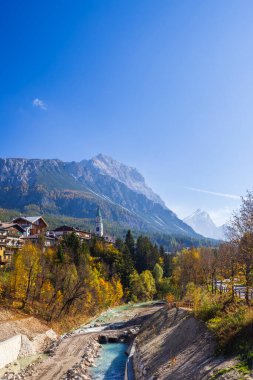 Livinallongo del Col di Lana sonbahar renklerini gösteriyor Biois deresi akıyor ve arka planda Dolomitler yükseliyor.