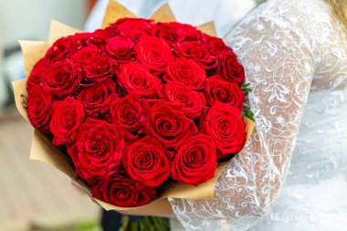 Beyaz elbiseli bir gelinin elinde güzel bir buket kırmızı gülle düğün gününde aşkı ve romantizmi simgeliyor.