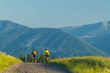 Slovakya 'nın Liptovsky Mikulas şehrinde çakıllı bir yolda bisiklet süren iki bisikletçi manzaranın tadını çıkarıyorlar.
