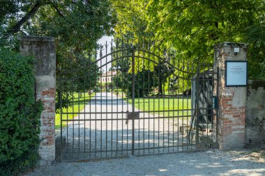 İtalya, Venedik 'te kapalı dövülmüş demir bir kapıdan bir kır evine giden çakıl yolu çevreleyen yemyeşil çimenler ve ağaçlar.