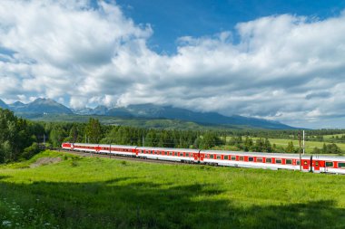 Slovakya 'da Strba yakınlarından geçen yolcu treni ve güneşli yaz gününde arka planda Yüksek Tatras dağları