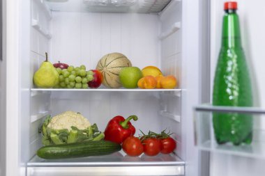 Açık buzdolabında taze meyve, sebze ve bir şişe meşrubat var.