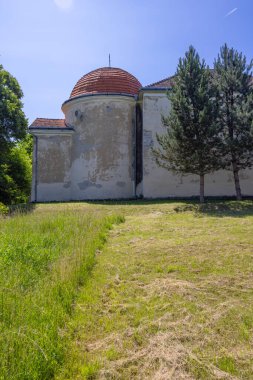 Slovakya 'nın Erkek Kosihy şehrinde ağaçlar ve çimlerle çevrili kırmızı kiremitli ve yıpranmış duvarları olan köşk.