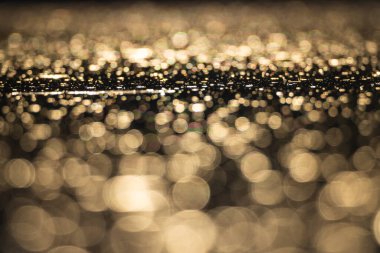 Soyut bulanık altın bokeh karanlık su yüzeyine yansıyarak güzel bir arkaplan oluşturuyor.