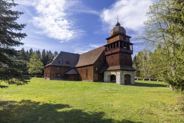 Slovakya 'nın Liptovsky bölgesindeki Svaty Kriz' in ahşap eklem kilisesi mavi bulutların altında yeşil bir çayırda duruyor.