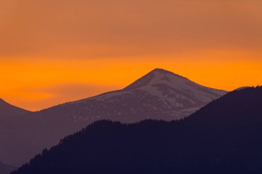 Karla kaplı dağ zirvesi canlı bir günbatımının ılık parıltısıyla güneşleniyor, Slovakya 'da nefes kesici bir manzara yaratıyor.