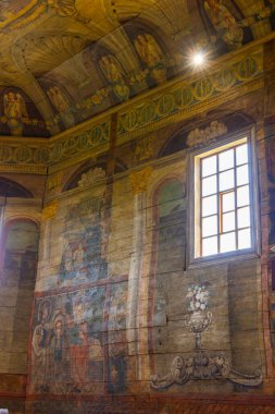 Polonya Haczow 'daki ahşap bir gotik kilisenin içindeki renkli dini resimler ve dekorasyonları aydınlatan pencereden süzülen güneş ışığı.