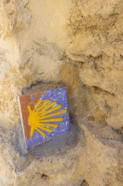 Sarı deniz tarağı kabuklu renkli fayans, Camino de Santiago sembolü, Castrojeriz, Burgos, İspanya 'da taş bir duvara gömülü.