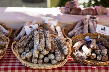 Nyons, Drome, Fransa 'daki bir çiftçi pazarındaki kareli masa örtüsünün üzerindeki hasır sepetlerde çeşitli Fransız sosislerinin görüntüsü