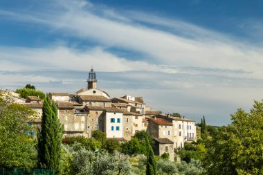 Fransa 'nın Drome kentindeki büyüleyici Venterol köyünün manzarasında geleneksel taş evler, canlı yeşillikler ve bulutlu mavi gökyüzünün arka planına karşı tarihi bir kilise kulesi sergileniyor.
