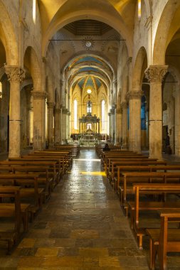 Massa Marittima cathedral interior with stone columns, vaulted arches, distant altar, and empty pews