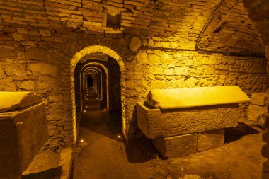 Ancient stone tunnel displaying sarcophagi, lit by warm underground lighting