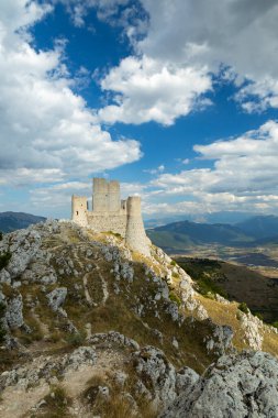 Rocca Calascio kalesi İtalya 'da canlı mavi bir gökyüzünün altında kayalık bir dağın tepesinde duruyor.