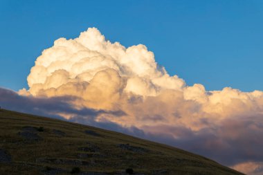 Altın kümülüs bulutları gün batımında kırsal kesimdeki kuru bir tepenin üzerinde birikiyor.