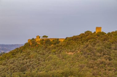 Pienza tepe binaları, aralarında antik bir duvar ve yemyeşil ağaçlar arasında kule, akşam ışığı ile yıkanmış