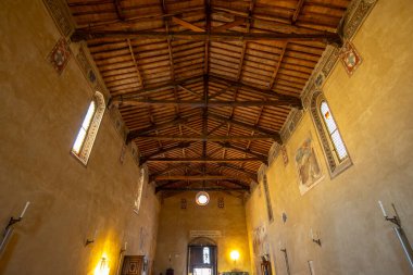 Ancient church interior featuring a traditional wooden ceiling, windows, and murals in Pienza, Italy