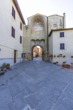 Historic archway with fresco and cobblestone piazza in charming Italian town