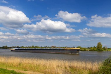 Lek Nehri 'nde mavi gökyüzünün altında, Lopik, Utrecht, Hollanda' da bulutları olan bir kargo gemisi.