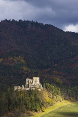 Likavka Kalesi, sonbaharda dramatik bir gökyüzünün altındaki orman tepesinde duruyor.
