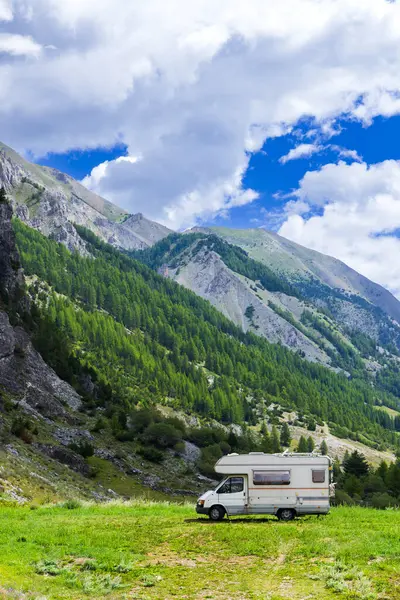 Argentera, Piedmont, İtalya 'da dağları ve ağaçları olan yeşil bir arazide park etmiş bir karavan.