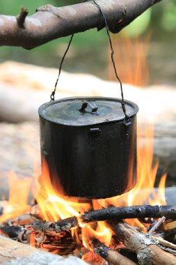 Kamp ateşinde yanan odunların üzerinde tütsülenmiş turist çaydanlığı.