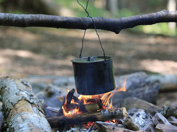 Ormanda kamp ateşi üzerinde tütsülenmiş turist çaydanlığı.
