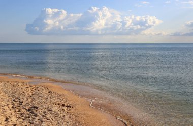 Denizde sakin bir yaz manzarası. Kumlu sahil ve gökte güzel bulutlar.