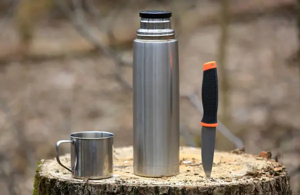 旅游设备 森林中木制树桩上的热水瓶 杯子和刀 免版税图库图片