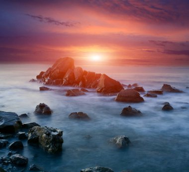 Akşam manzarası, deniz suyundaki taşların üzerinde gün batımı.