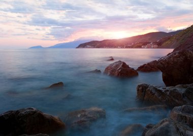Günbatımı arka planında taşlarla dolu deniz manzarası. Kırım dilinde konuş.