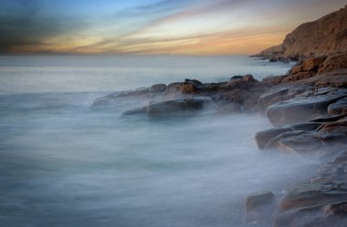 Deniz suyunda taşlar olan gün batımı manzarası.