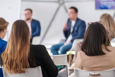 Plastik sandalyelerde oturan ve açık konferans sırasında hoparlörleri dinleyen isimsiz iş kadınları