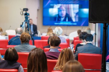 Kırmızı deri koltuklarda oturan ve online iş semineri sırasında hoparlörlerin video konuşması yapan tanınmamış izleyiciler.