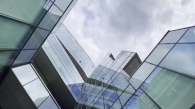 Tavanın altından, bulutların altında geometrik cepheli modern binanın yansıtıcı cam duvarları görünüyor.