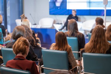 Salondaki sandalyelerde oturan ve iş konferansı sırasında konuşmacıları dinleyen isimsiz kadın izleyiciler.