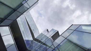 Tavanın altından, bulutların altında geometrik cepheli modern binanın yansıtıcı cam duvarları görünüyor.