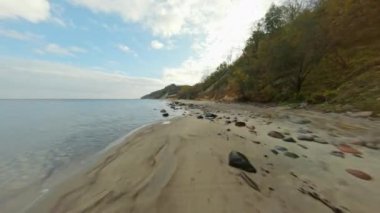 Sonbahar sabahı bulutlu mavi gökyüzüne karşı deniz suyu ve tepenin arasında kayalar bulunan kumlu kumlu kumsal görüntüsü.