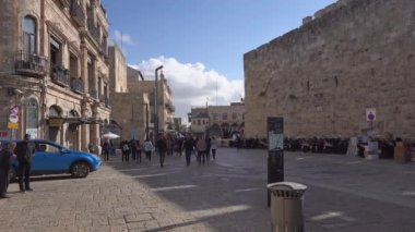 Ierusalim, İsrail - 12 Kasım 2022: İsrail 'in Eski Kudüs kentindeki tarihi binanın ortasında kaldırımda yürüyen kalabalığın yanında giden mavi arabanın el kamerası