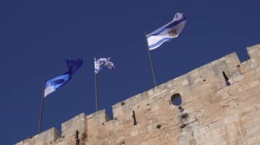 İsrail bayraklarının statik çekimlerinden yıllanmış taş duvarın tepesindeki rüzgarda bulutsuz mavi gökyüzüne doğru dalgalanıyordu.