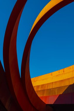 Günışığı turuncu duvarı ve bulutsuz mavi gökyüzünün altındaki çağdaş bina halkalarından.