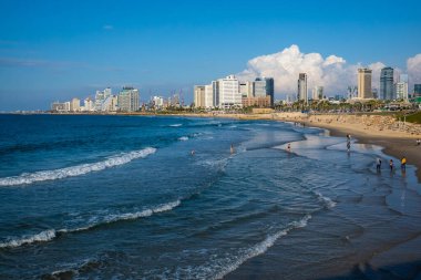İsrail 'in Tel Aviv kentindeki bulutlu mavi gökyüzüne karşı kumlu sahilde deniz dalgaları etrafında yürüyen turistlerin insansız hava aracı görüntüsü