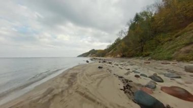 Fırtınalı bir kırsal günde bulutlu gökyüzüne karşı dalgalanan deniz kenarındaki lastik izleriyle tepenin ve kumlu plajın görüntüsü.
