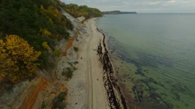 Fırtınalı bir kırsal günde bulutlu gökyüzüne karşı dalgalanan deniz kenarındaki lastik izleriyle tepenin ve kumlu plajın görüntüsü.