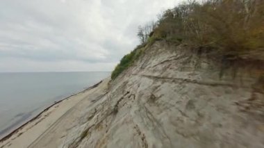 Fırtınalı bir kırsal günde bulutlu gökyüzüne karşı dalgalanan deniz kenarındaki lastik izleriyle tepenin ve kumlu plajın görüntüsü.