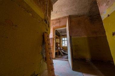 Tahta kapıyı açtı. Gündüz vakti yıpranmış terk edilmiş bir binanın yıkılmış odasına açılıyor.