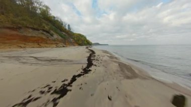 Fırtınalı bir kırsal günde bulutlu gökyüzüne karşı dalgalanan deniz kenarındaki lastik izleriyle tepenin ve kumlu plajın görüntüsü.
