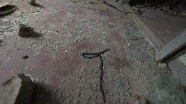 Ekin sahibinin el kamerasıyla çekilen bu fotoğraf, yıpranmış odada döşemeli zemine basıyor, toz ve atıklarla birlikte parlak cam kırıklarıyla birlikte.