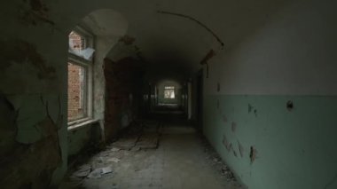 Handheld shot of walking in long dark hallway with room entrances inside of aged abandoned building in decay